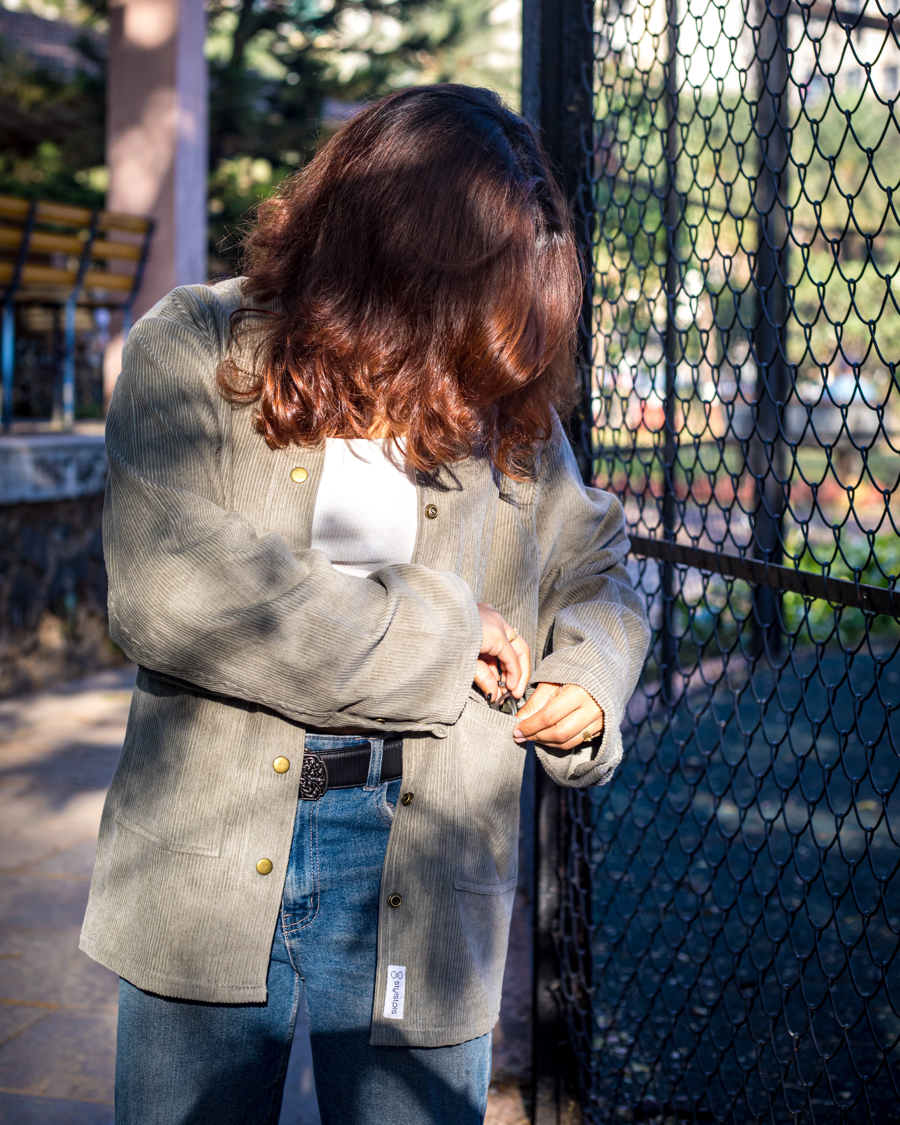 Person wearing a grey blazer and blue jeans standing near a fence.