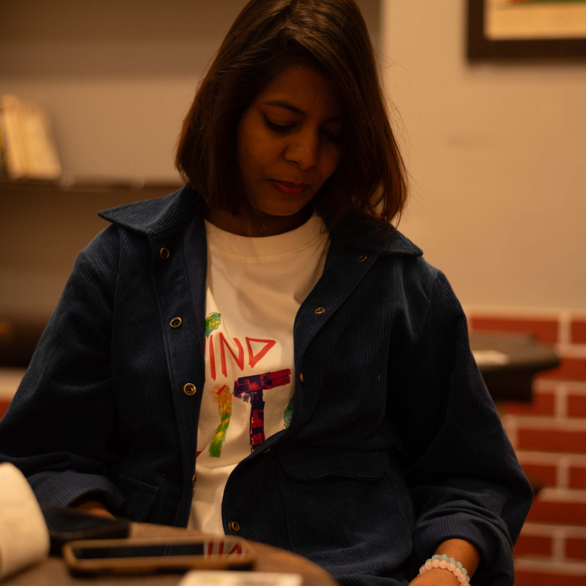 Woman sitting at a table in a casual setting with a brick wall and framed picture in the background.